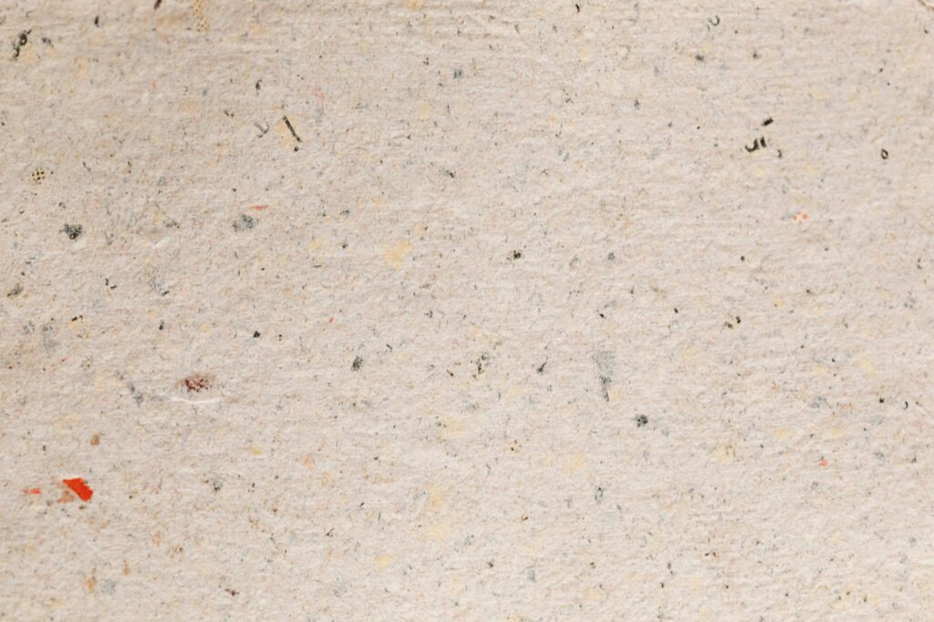 Close-up texture of recycled paper, featuring natural speckles and rough surface.